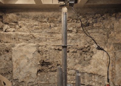 Artigiano al lavoro su piedistallo metallico per scultura di giovane atleta in ambiente archeologico con pareti in pietra.