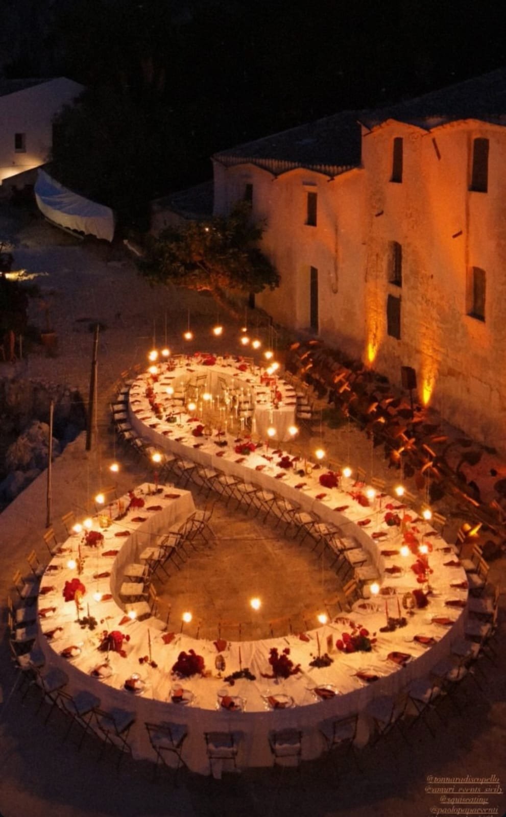 Tavolo a forma di infinito per 100 persone con illuminazione a candele, allestimento scenografico per eventi e matrimoni
