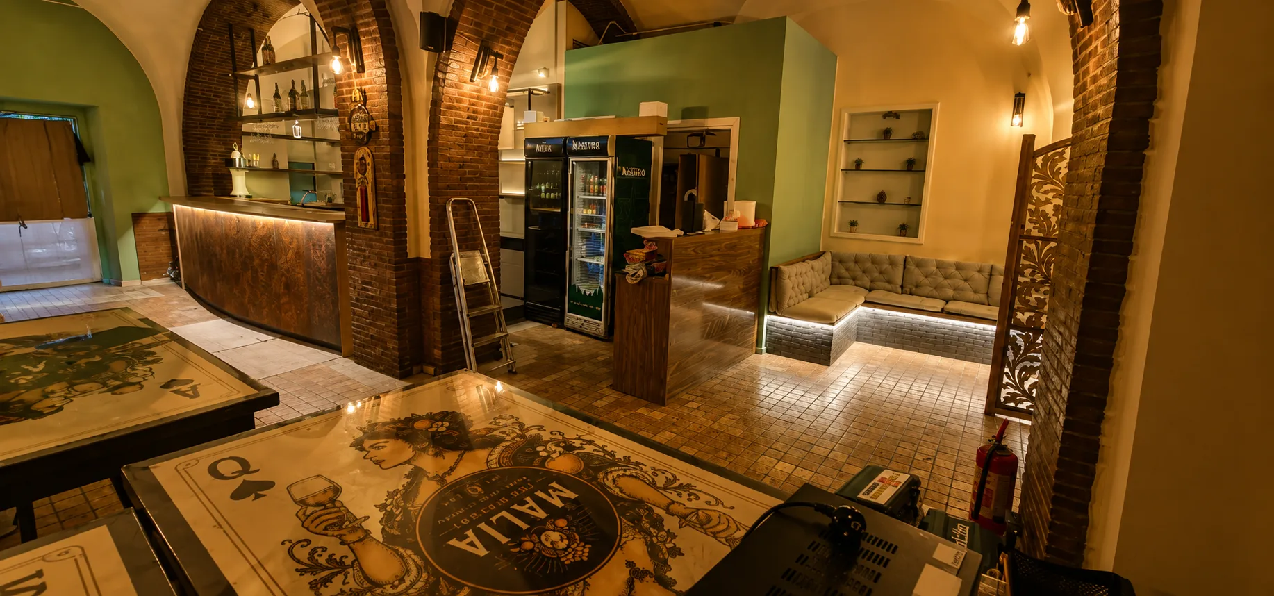 Malìa Pub Bistrot – Vista d'insieme Vista d'insieme del Malìa Pub Bistrot dopo il restyling realizzato da Skenarte con bancone su misura, retrobanco illuminato e area privè